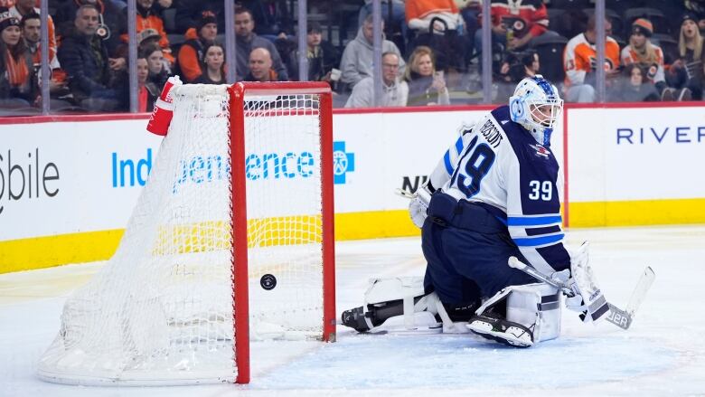 A puck going into a goal while the goalie looks back at it.