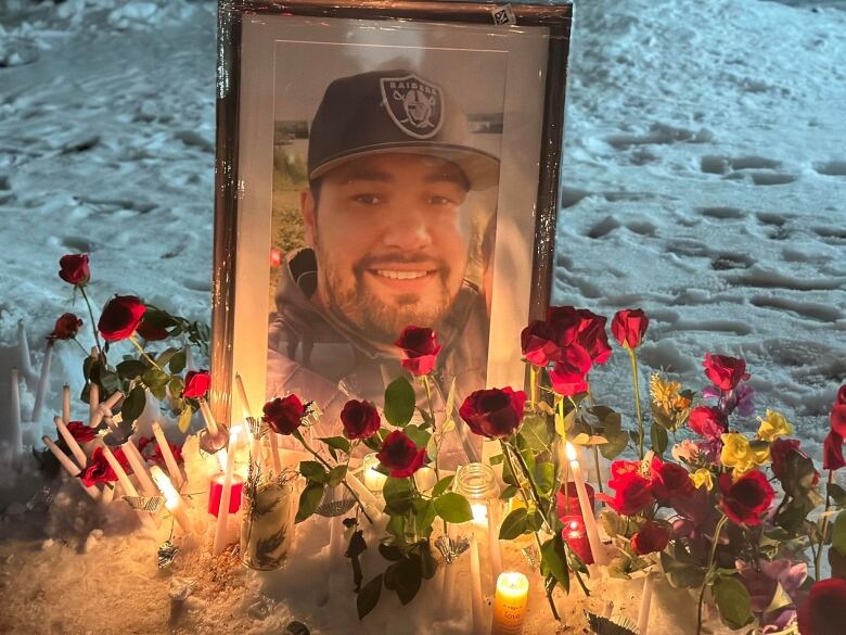 Roses and candles sit front of a framed photo of a man with a beard and black baseball cap.