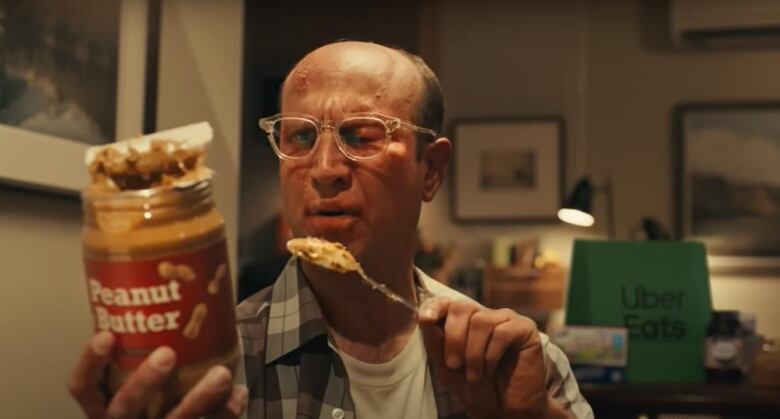 A man with a swollen eye and hives breaking out on his forward reads the label of a peanut butter jar. 