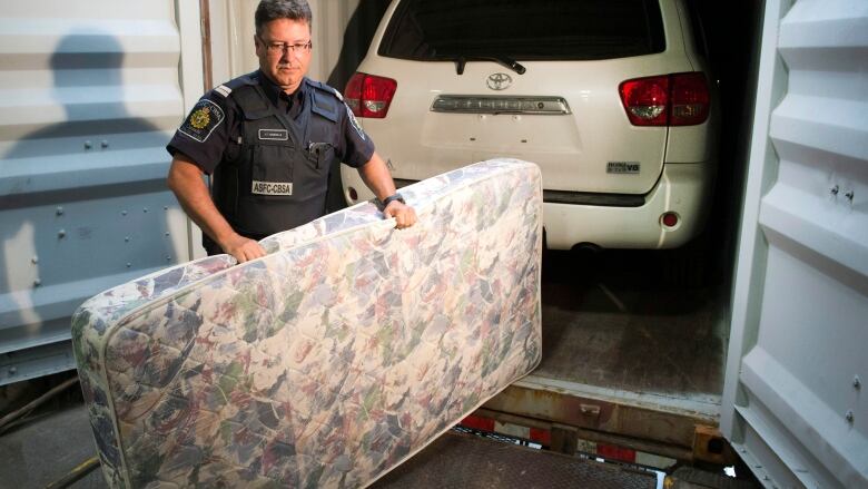 A police officer stands in front of a vehicle parked in a shipping container.