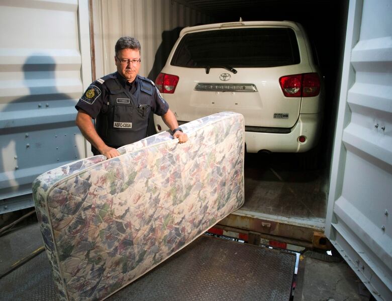 A police officer stands in front of a vehicle parked in a shipping container.