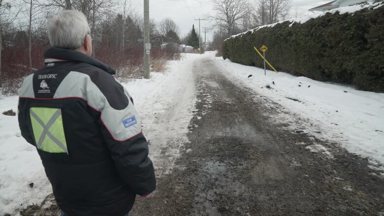 A man with his back turned looking at a gravel trail.