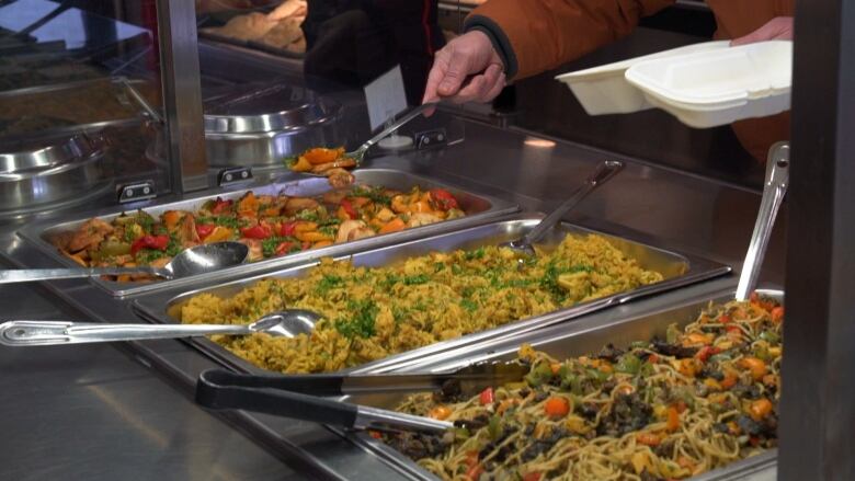 A person's arm reaches to get food from a hot food buffet. 