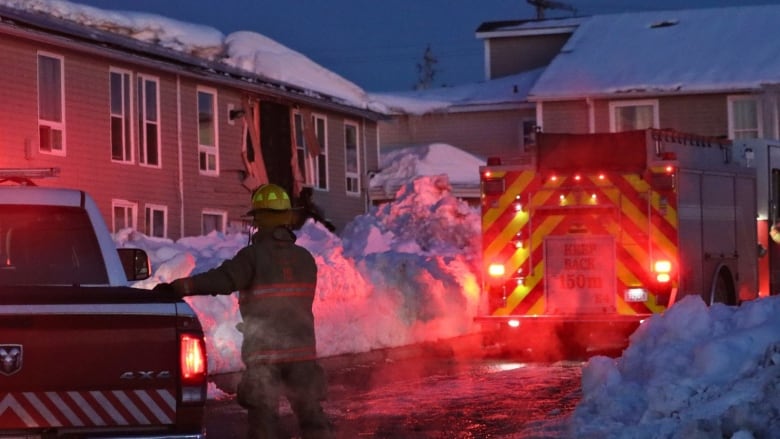 a firefighter stands in front of an apartment building at night.