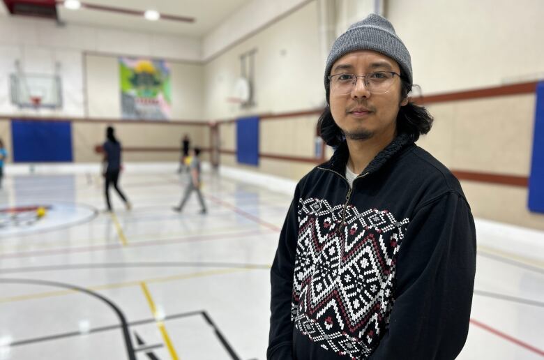 A man at an indoor basketball court, posing for a picture while children play in the background.