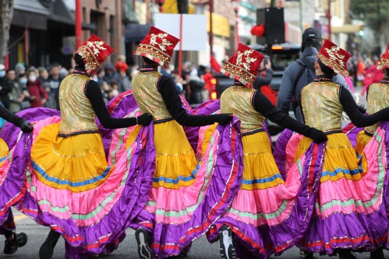 A row of women with colourful costumes dancing in a line on a street.