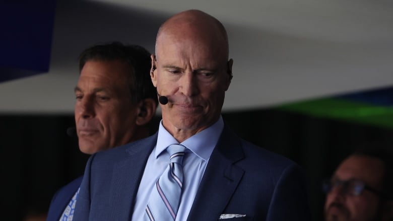 Men's broadcaster watches a hockey game from a broadcast booth. 