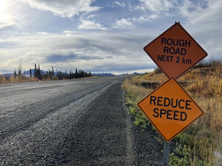 Signs beside an empty roadway warn of rough road ahead and advise drivers to reduce speed.