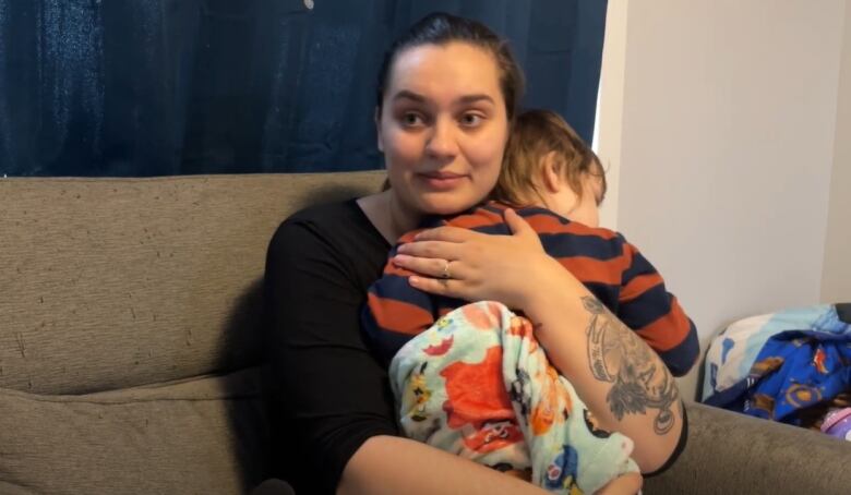 A woman sitting on a couch cuddles a young boy.