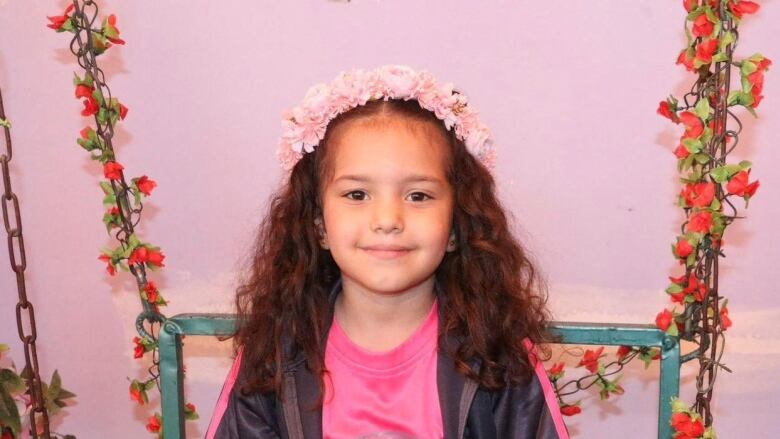 A child wearing a flower crown smiles while posing for a photo.