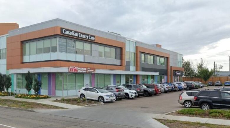 Vehicles are parked in a row in front of a silver and orange building.