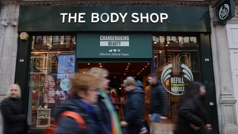 People walk in front of a store front that says The Body Shop