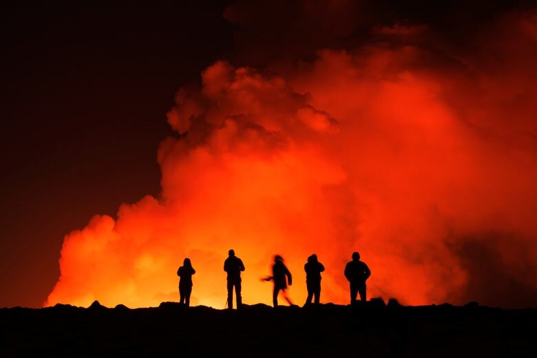 A group stands in shadow in front of an erupting Iceland volcano.