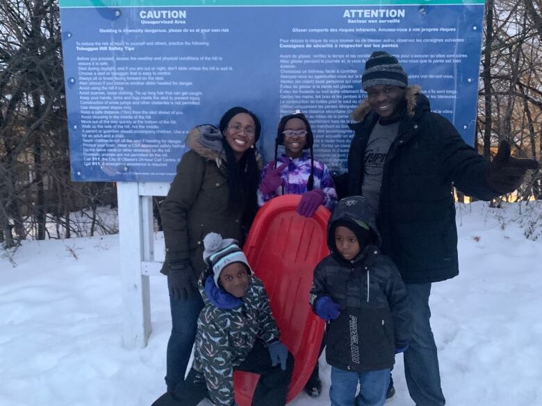 A family smiles holding a sled at the top of a toboggan hill.