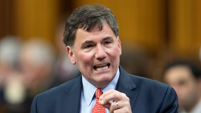 A man in a blue suit and red tie speaks in the House of Commons.