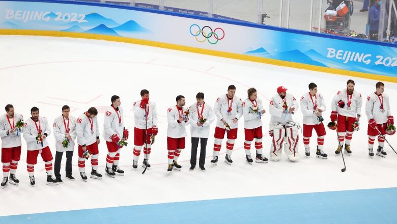 Men's hockey players standing on ice after receiving medals.