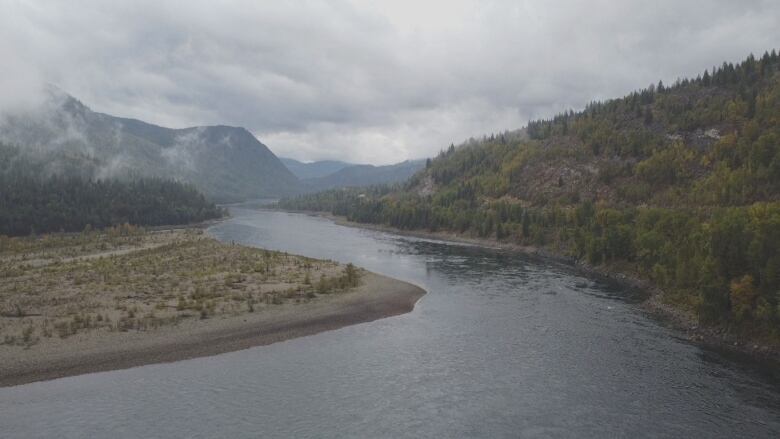 A large river on a cloudy day with mountains on either side. 