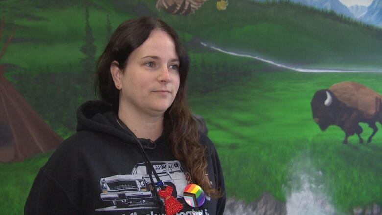 A woman in a hoodie standing in front of a mural painting of a field with a bison on it.