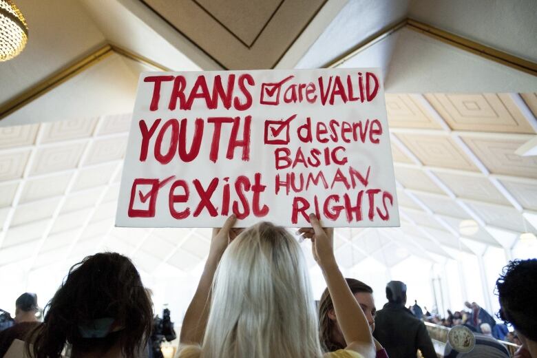 A person is shown from behind holding a sign that reads: 