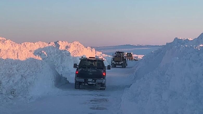 Trucks drive down a snow covered road.