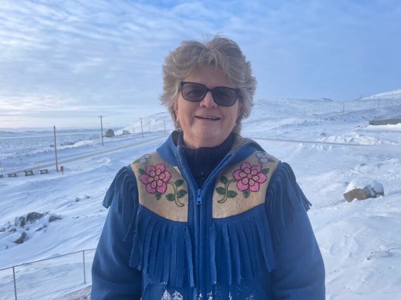 A woman in a blue coat stands outside with snowy, barren hills visible behind her.