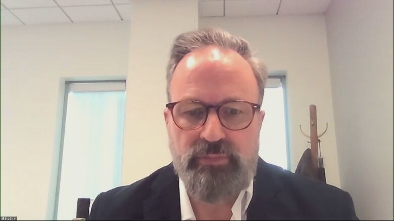 A man with short hair and glasses and a beard speaks into a web camera.