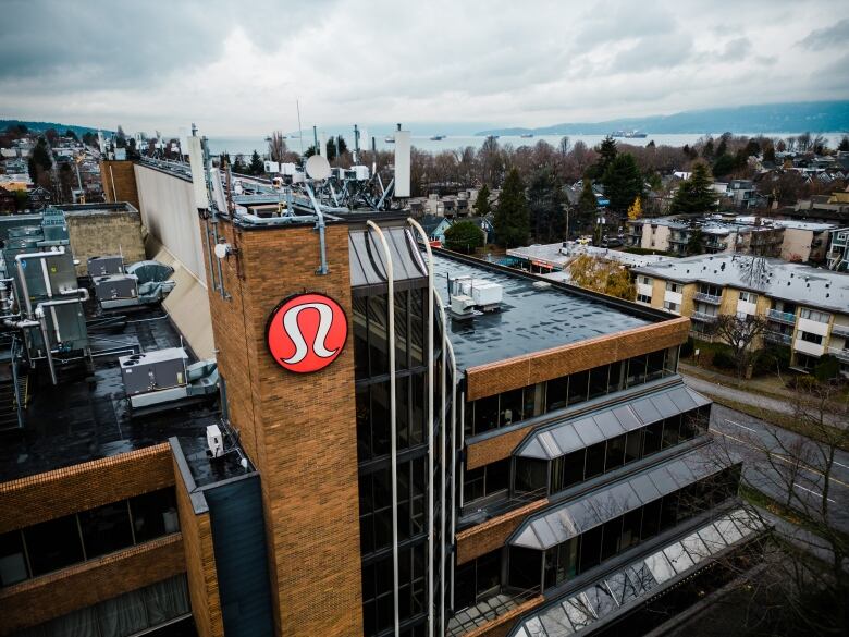 The Lululemon logo is affixed to a large brick building, photographed from above and overlooking a neighbourhood.