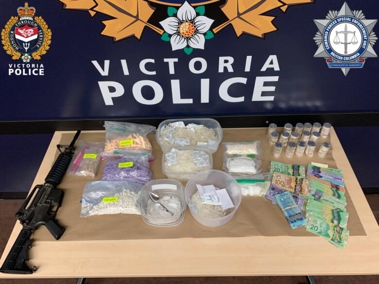 A table in front of a Victoria Police logo shows a gun, multiple containers filled with drugs and a stack of paper money.