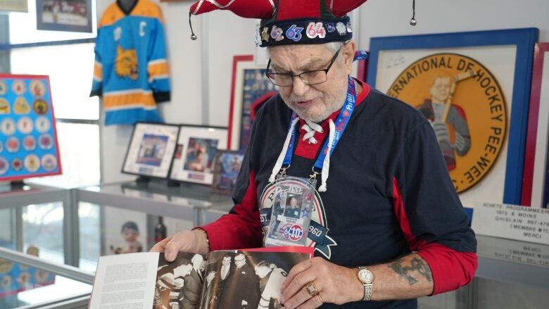 A man wearing a hockey shirt holds a photo printed in a magazine. He is standing in a hockey museum. 