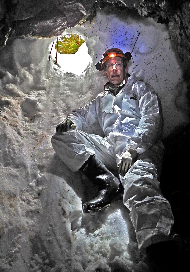 A man in a full hazmat suit and hard hat in a snow and ice-encrusted cave opening. 