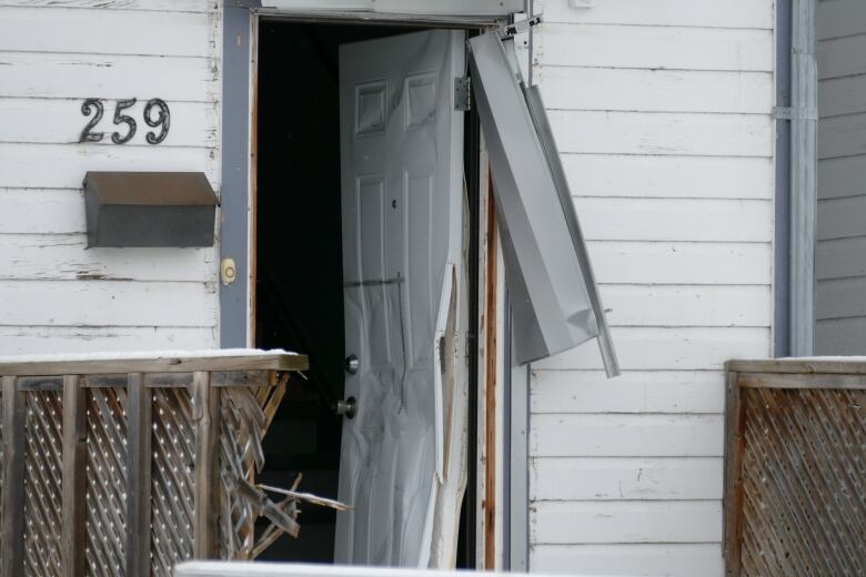 A front door to a home is open and dented.