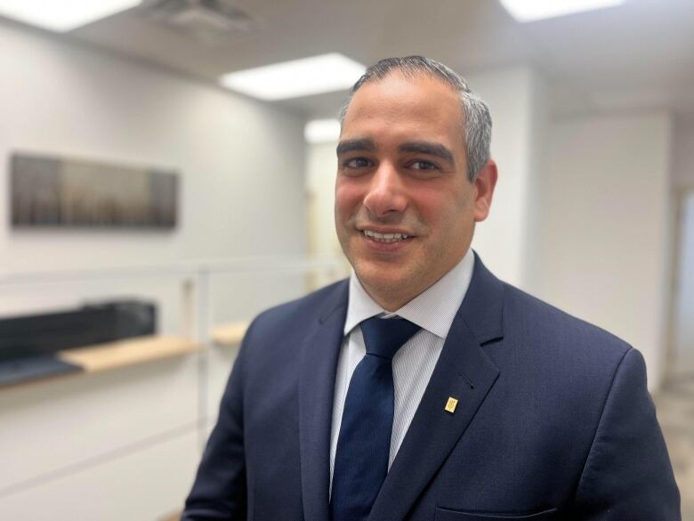 A man in a grey suit looking at the camera in an office 