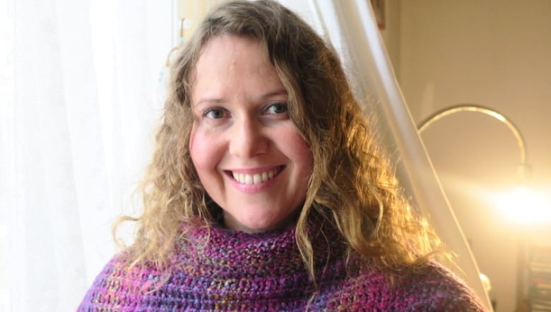 A woman in a purple knit sweater smiles for a photo.