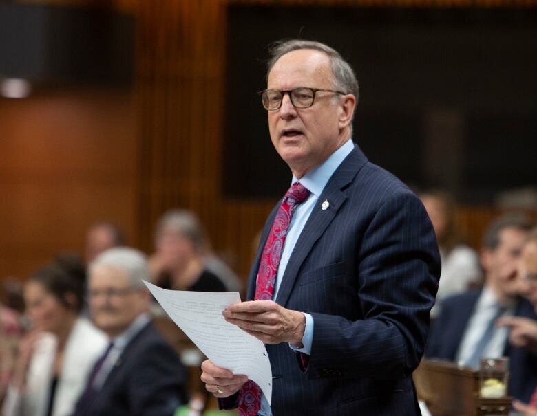 A man in a blue suit reads from a sheet of paper.