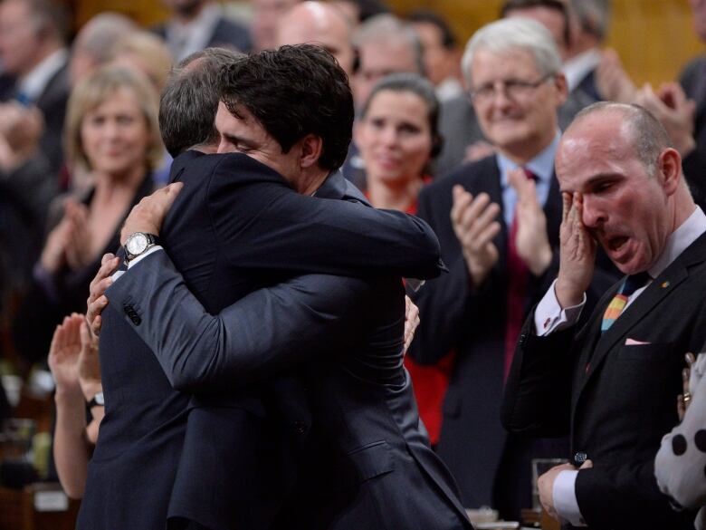 Two men in suits embrace.