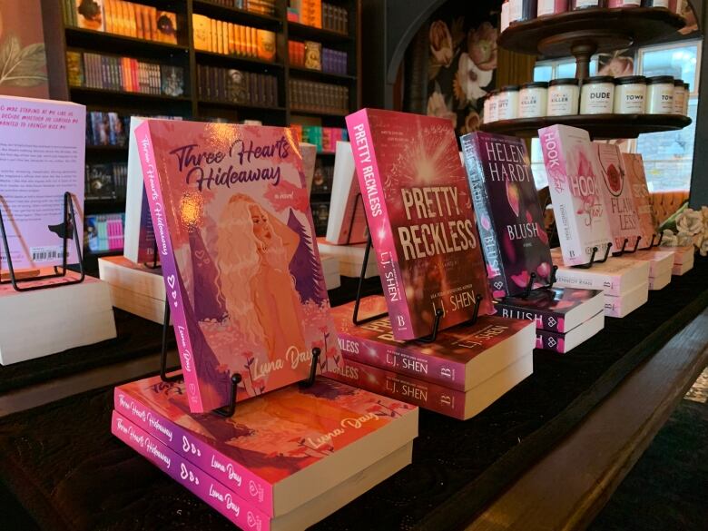 Books are lined up on a table, with a display of candles to the right and more bookshelves in the background.