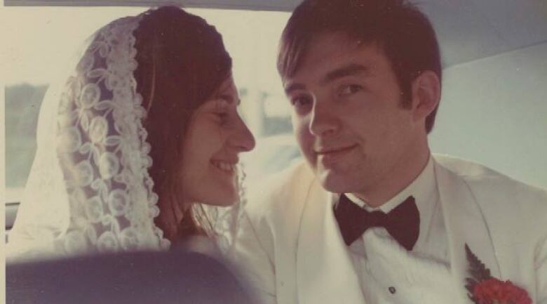 A man and woman sitting in a car. The woman is wearing a veil and smiling and the man who is wearing a suit. 