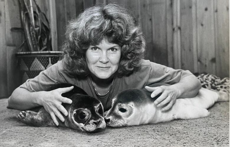 A black and white photo os a woman wit two dead seal specimens. 