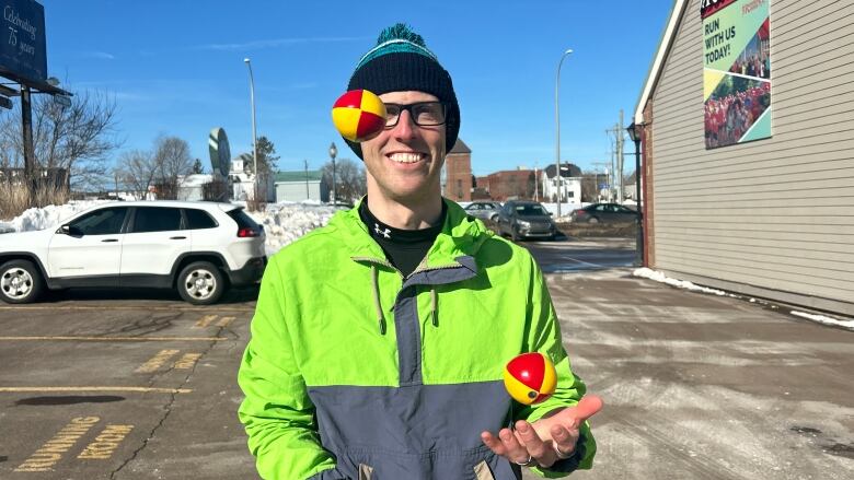 A white man wearing a tuke and glasses. He is juggling three balls.