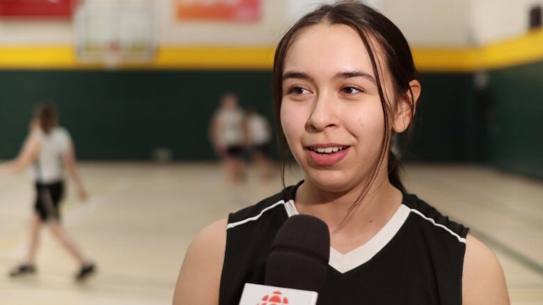 A girl in a uniform smiles while talking into a microphone. 