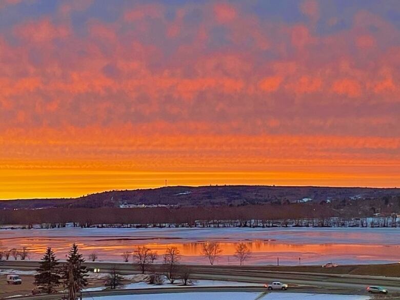 An orange and yellow sky over a snowy river and hill.