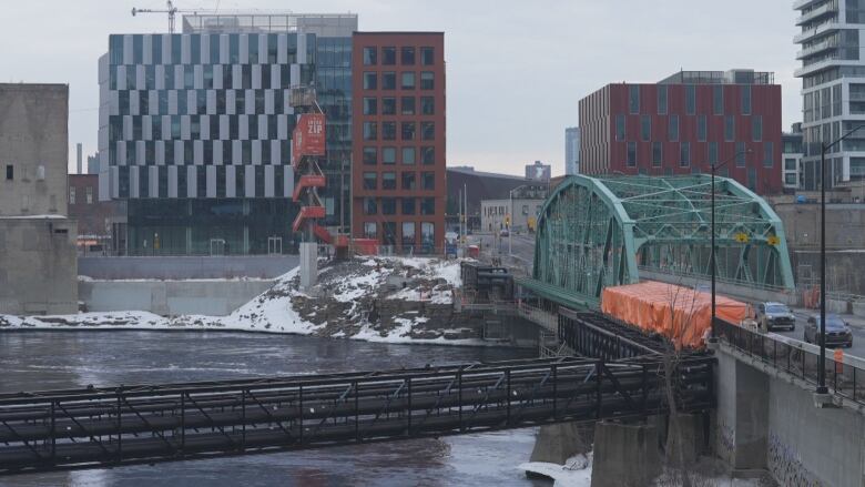 Black pipes in foreground in front of green bridge over river with towers in the background