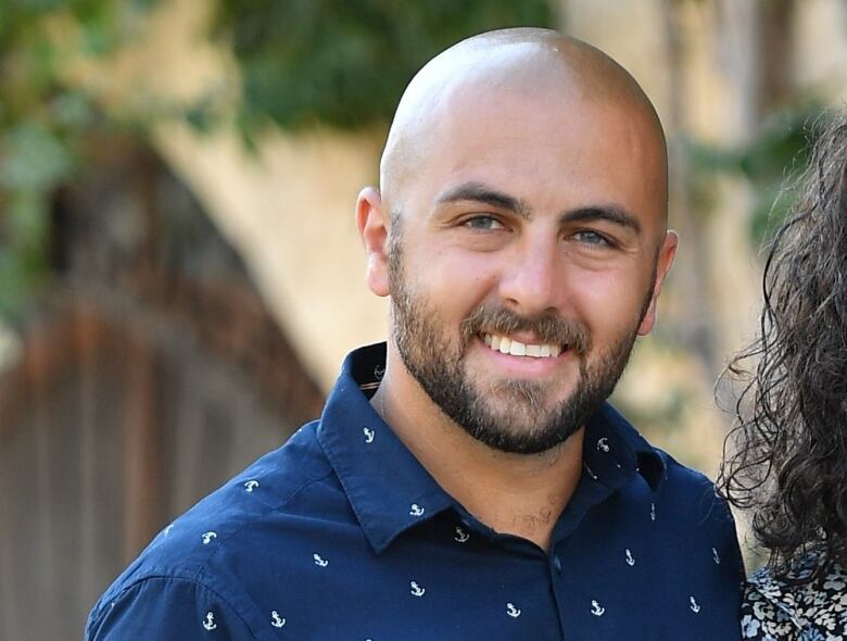 A bald-headed man in a blue shirt smiles at the camera.