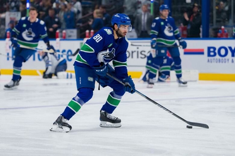 A South Asian man wearing a blue hockey uniform skates on the ice and plays with a puck.