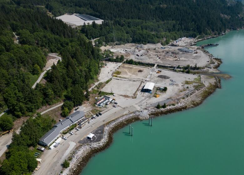 An industrial site with numerous portable buildings is seen from above next to a blue river.