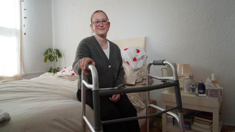 Young woman sits on bed with walker in front of her.