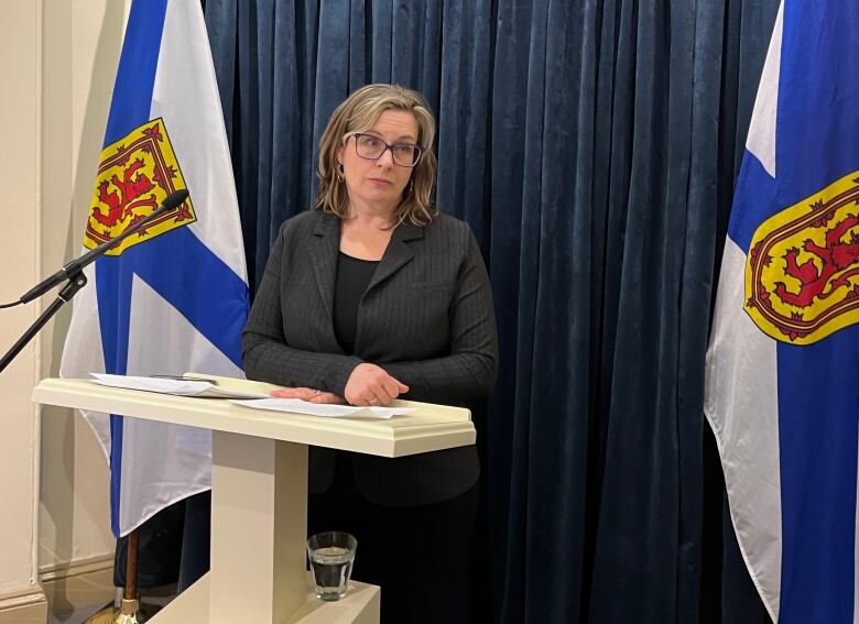 A woman with glasses stands at a podium.