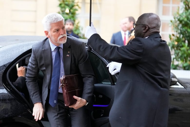 A bearded man in a suit gets out of a car.