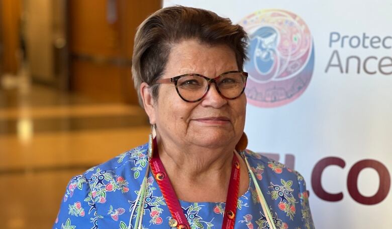 A woman with short brown hair and brown glasses is pictured smiling to the camera.