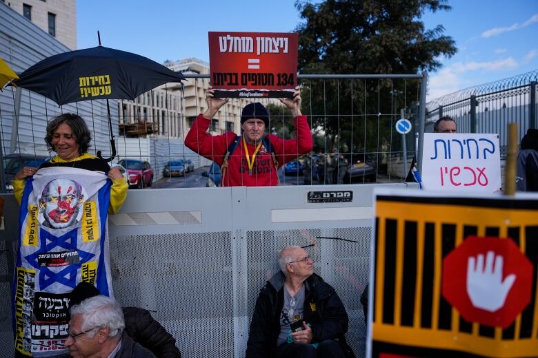 Two men and a woman hold signs and banners at an outdoor demonstration.